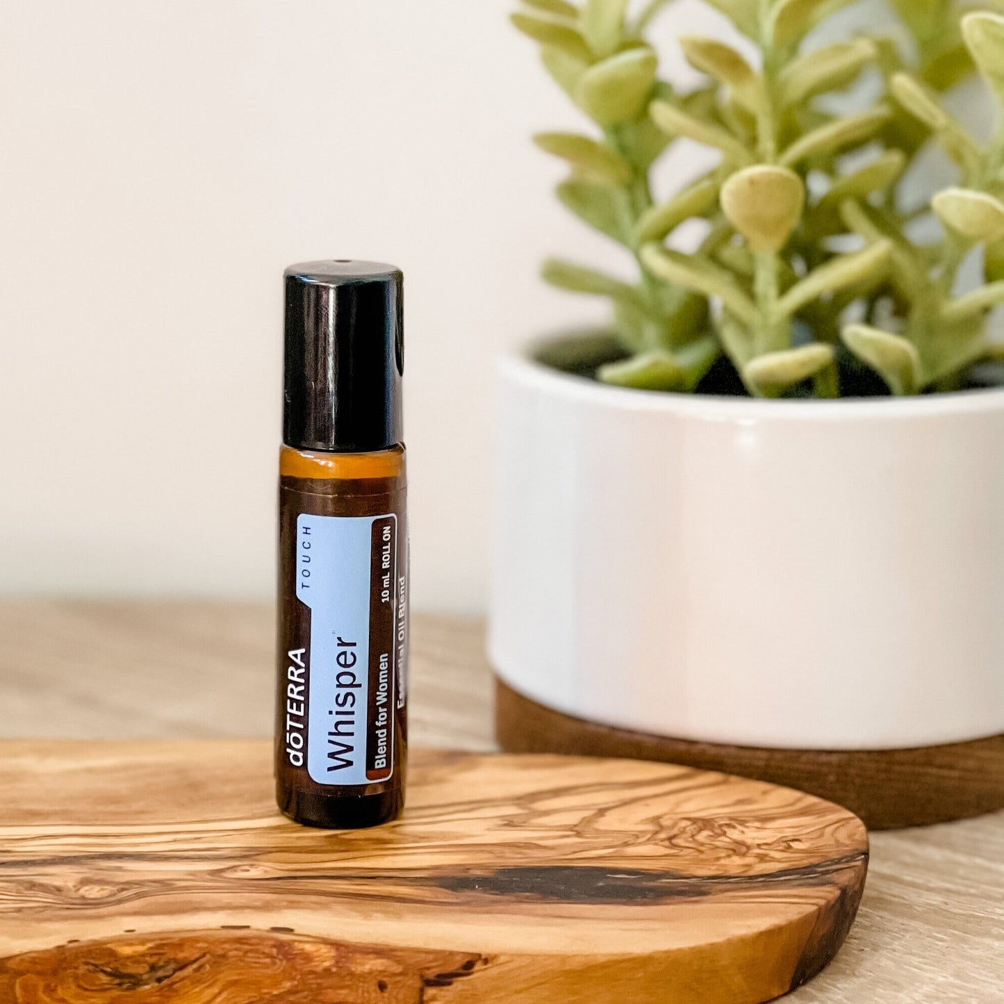 doTERRA Whisper essential oil roller bottle sitting on a wooden bench with a green plant behind.