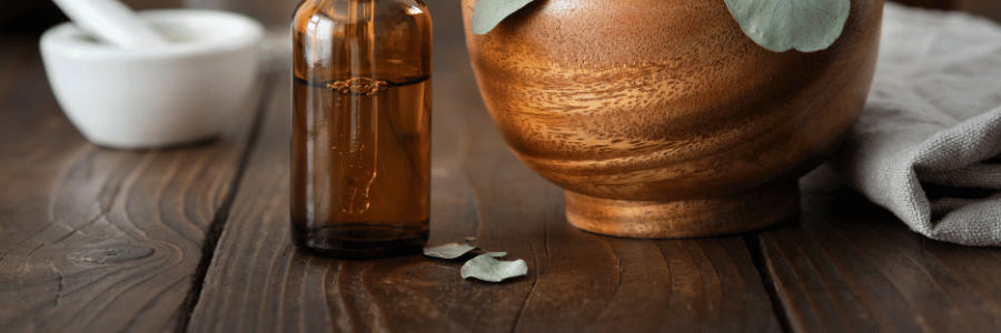 Amber glass bottle on a wooden surface with a wooden bowl and white cloth in the background
