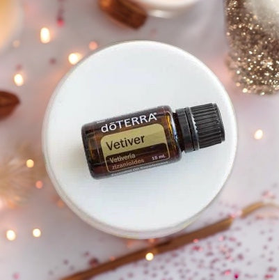 doTERRA Vetiver essential oil bottle on a white surface with blurred lights and cinnamon sticks in the background