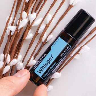 doTERRA Whisper essential oil roller bottle being held in the tips of fingers with natural elements behind