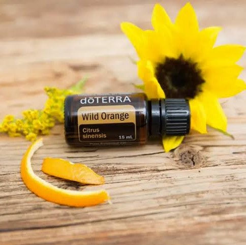 doTERRA Wild Orange essential oil bottle with a sunflower and orange peel on a wooden surface