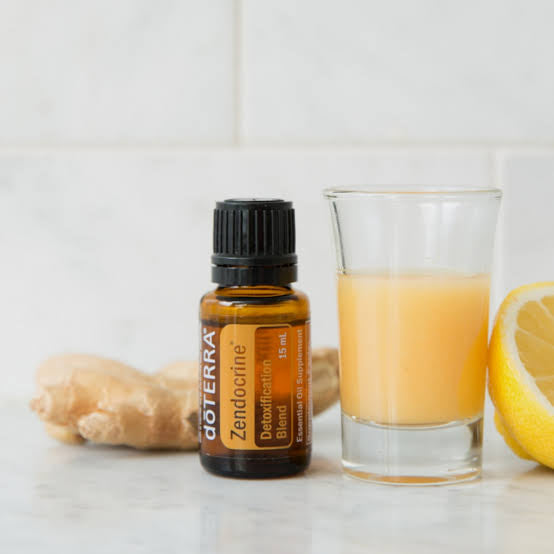 doTERRA Zendocrine essential oil bottle with a glass of orange juice, ginger root, and lemon on a white background