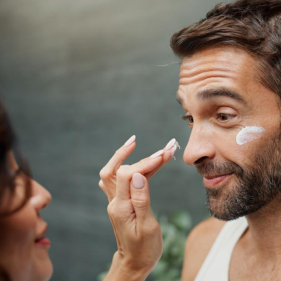 Person applying cream to another person's face with a blurred background