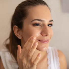 Woman applying cream to her face with a neutral background
