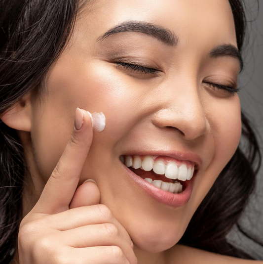 Woman applying cream to her face with a neutral background