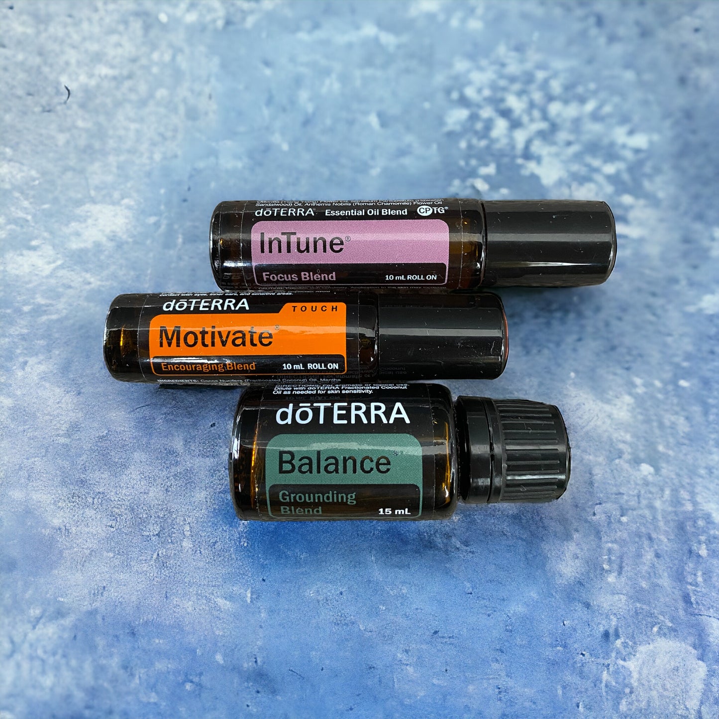 doterra Motivate, doterra Balance and doterra Intune Roll On on a bllue background.