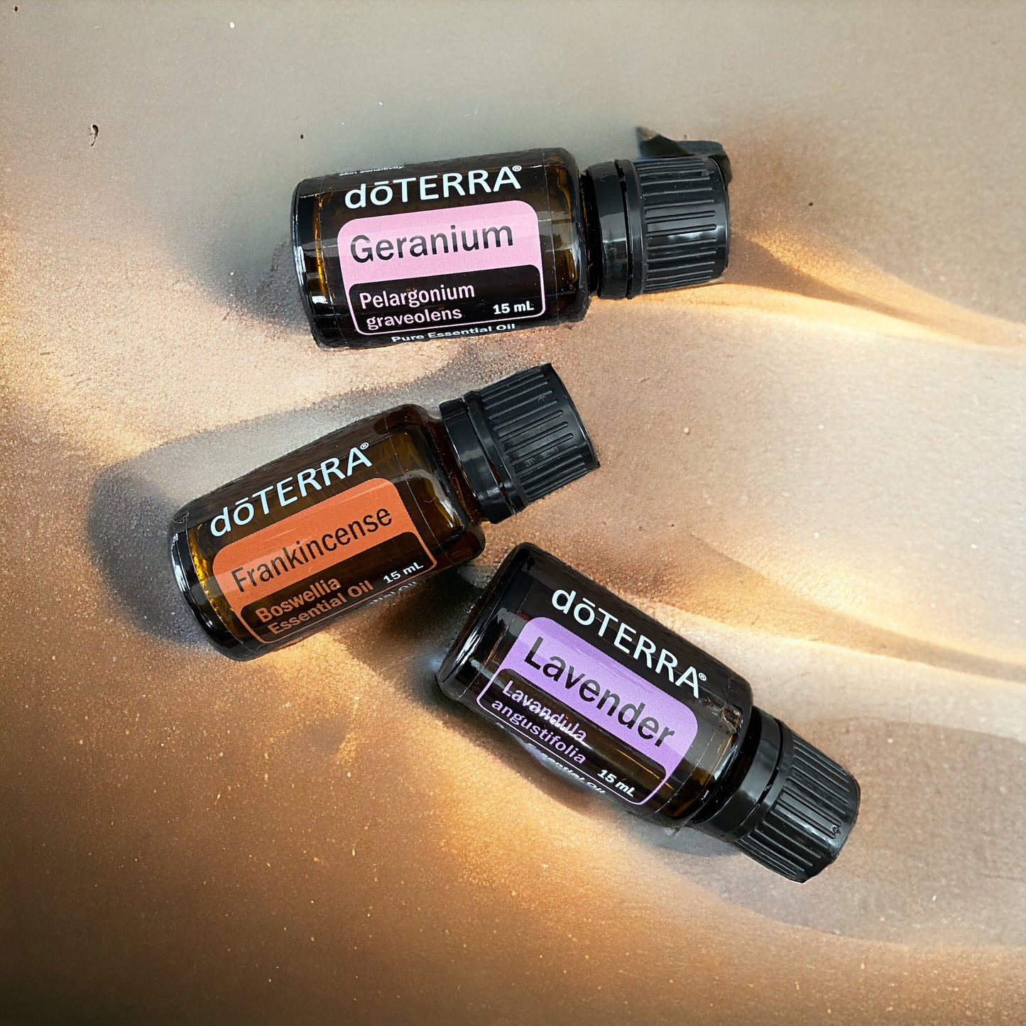 Three doTerra essential oil bottles, labeled Frankincense, Geranium, and Lavender, scattered on a golden background.