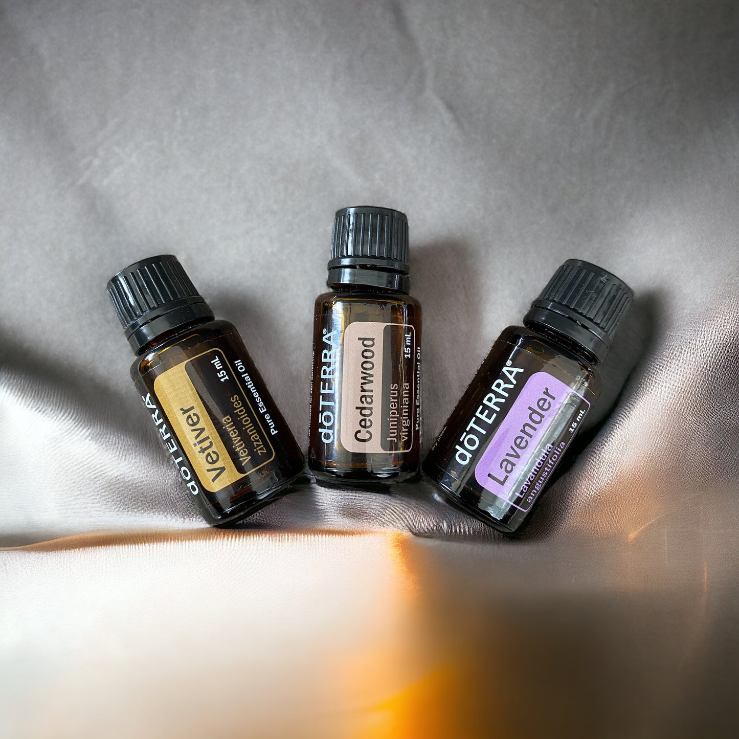 doterra vetiver, doterra lavender and doterra cedarwood essential oils laying on a silver sheet with golden light illuminating from below.