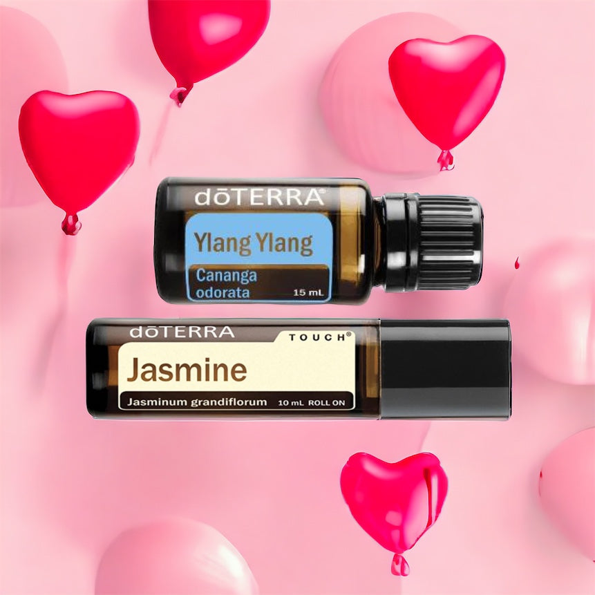 Two bottles of doTerra essential oils, one labeled Jasmine Touch and the other Ylang Ylang, set against a pink backdrop with pink hearts.