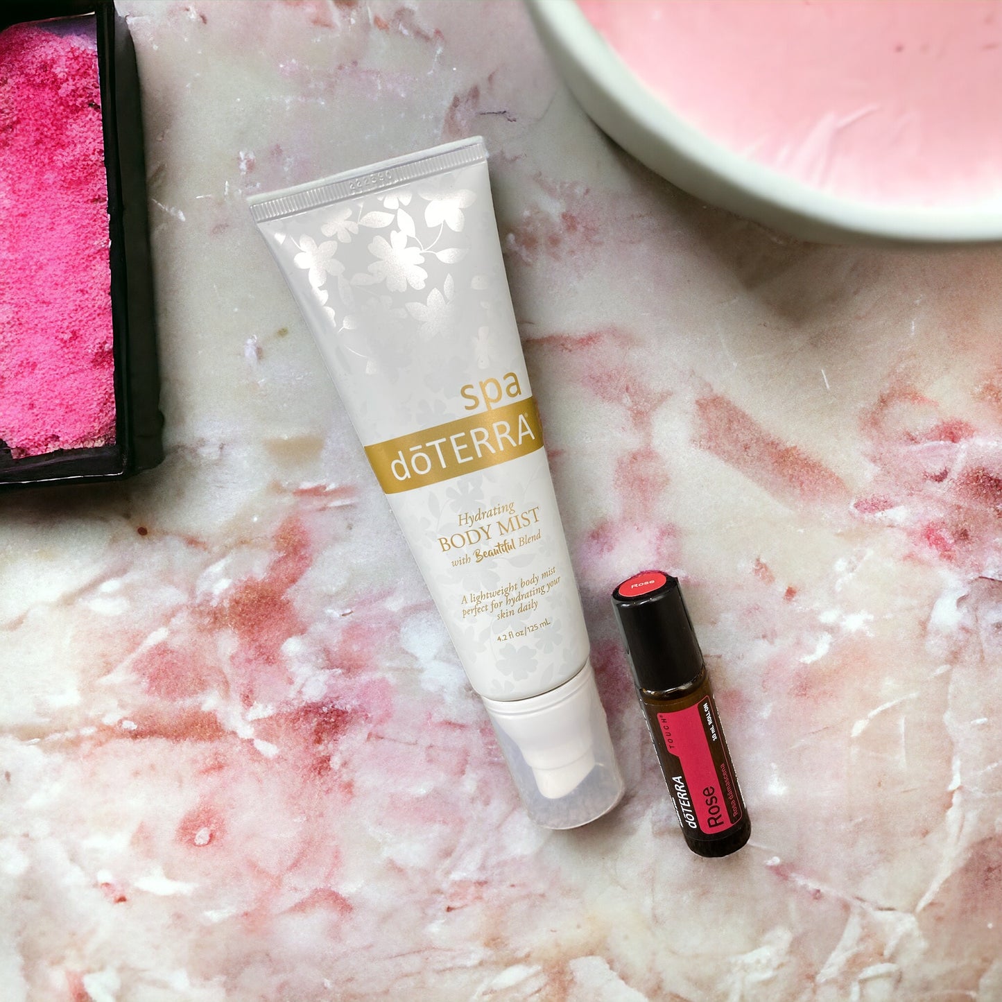 doterra hydrating mist and doterra rose touch against a pink and white marble countertop with pink elements surrounding.