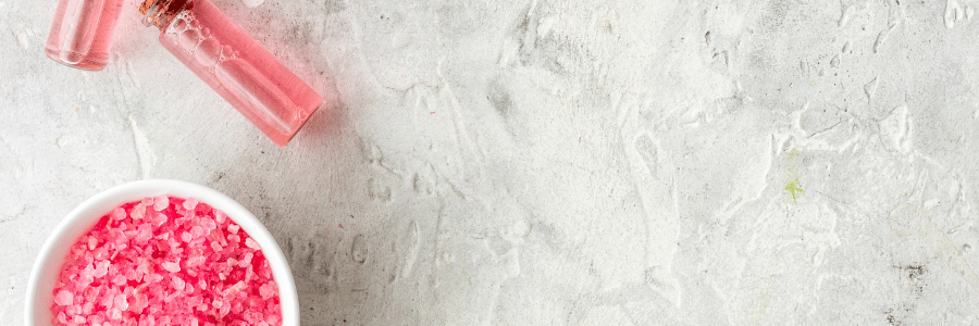 Pink lip gloss and bath salts on a textured white surface