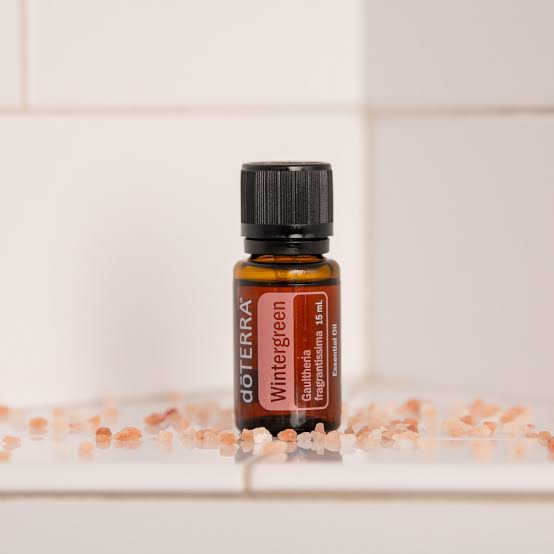 doTERRA Wintergreen essential oil bottle on a white surface with small decorative items.