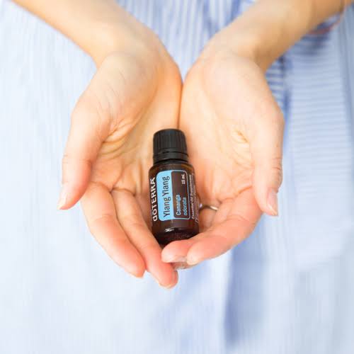 Hand holding a doTERRA essential oil bottle with a blurred background