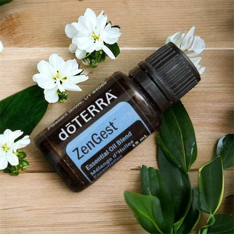 doTERRA ZenGest essential oil blend bottle on a wooden surface with white flowers and green leaves.