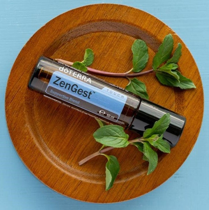 doTERRA ZenGest roller bottle on a wooden plate with green leaves against a blue background