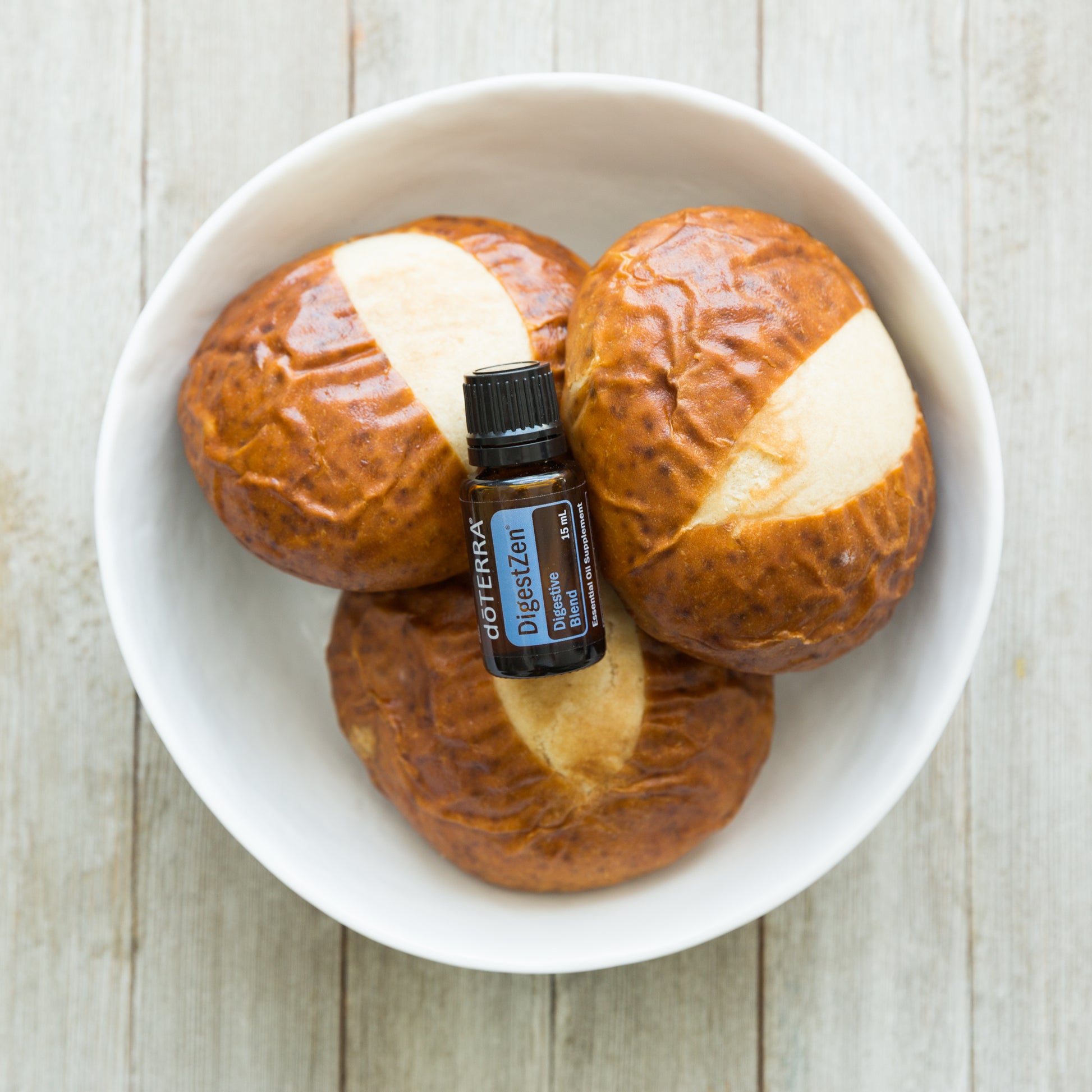doTERRA DigestZen essential oil bottle on pretzel buns with butter on a white plate.