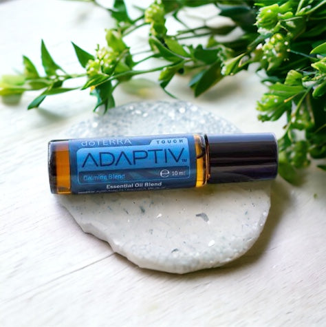doterra adaptiv touch laying on a rey stone with green leaves and flowers above
