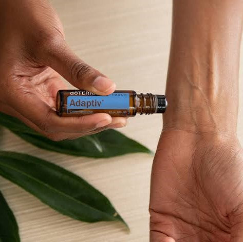 doterra adaptiv touch being rolled onto a wrist with green leaves below