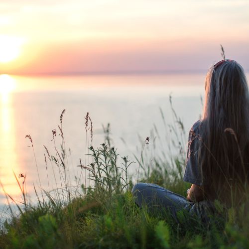 Woman meditating facing a sunset essential oils for anxiety relief – Natural rituals for calm and relaxation