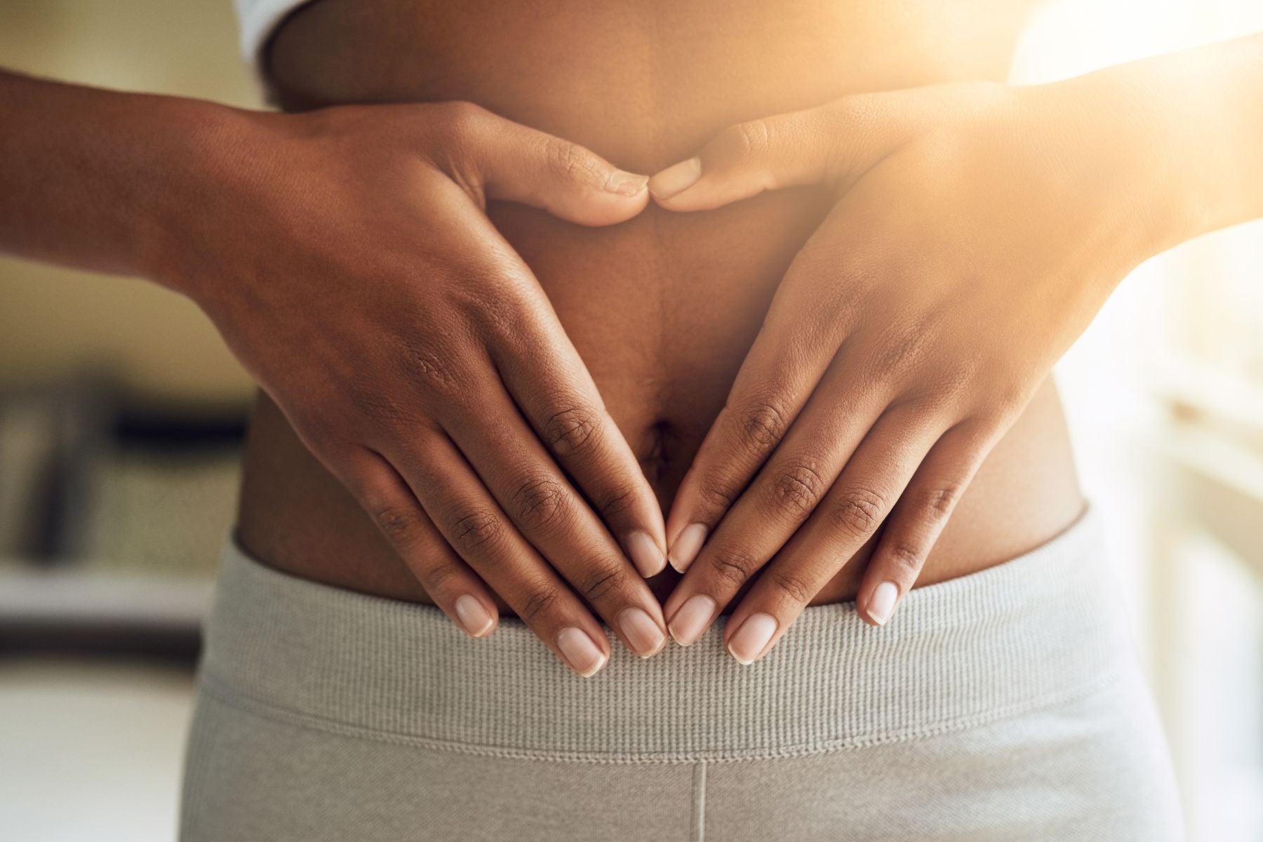 Love heart hands over a flat stomach – Symbolizing healthy digestion and wellness support.
