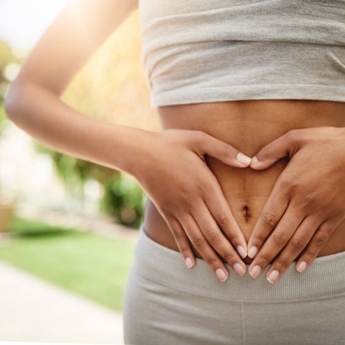 Hands in the space of a love heart over a bare flat stomach. Essential oils for healthy digestion and gut health.
