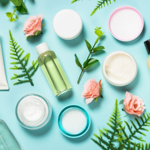 Scattering of beauty products and green foliage over a  blue background. Skin & Beauty ritual – Essential oils for radiant skin and natural beauty