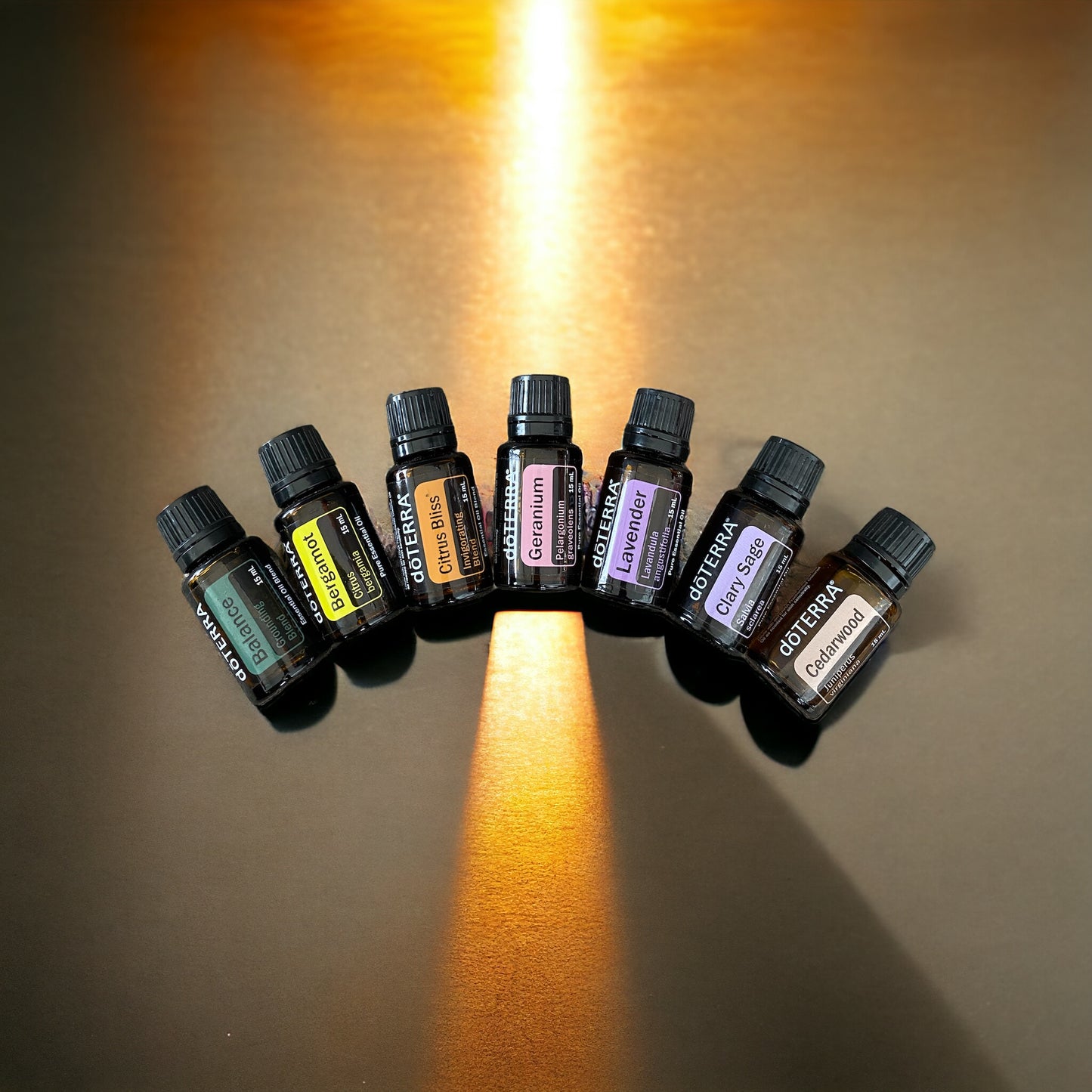 A selection of seven doTerra essential oil bottles, each representing a different color and scent, arranged in a rainbow shape on a gold background with evening light shooting through.