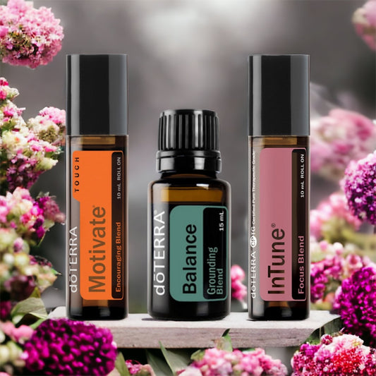 doterra Motivate, doterra Balance and doterra Intune Roll On standing on a marble platform surrounded by pink and green flowers.