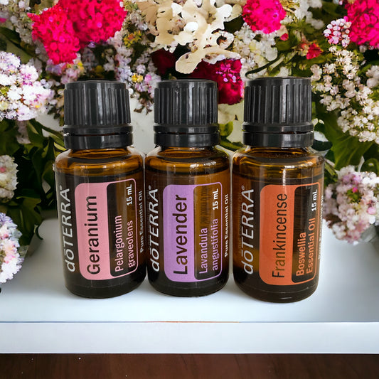 Three doTerra essential oil bottles, labeled Frankincense, Geranium, and Lavender, arranged side by side with a vase of flowers in the background.