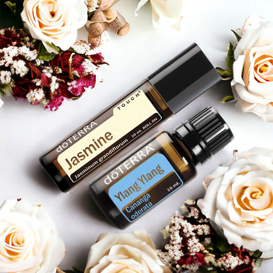 Two bottles of doTerra essential oils, one labeled Jasmine Touch and the other Ylang Ylang, set against a backdrop of flowers.