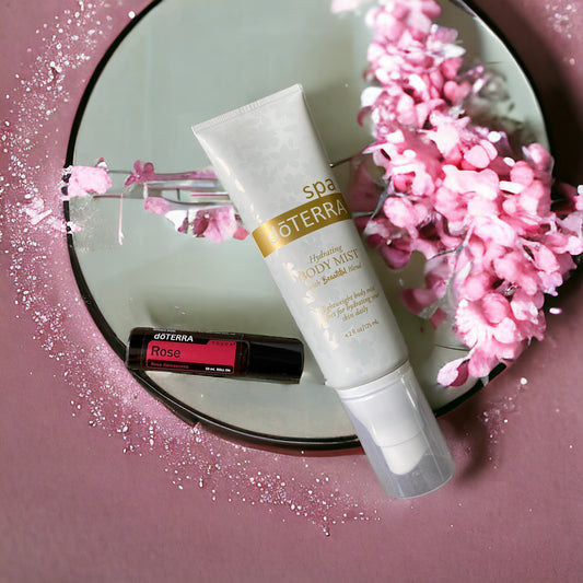 doterra hydrating mist and doterra rose touch laying on a circular mirror against a pink background with pipnk flowers.